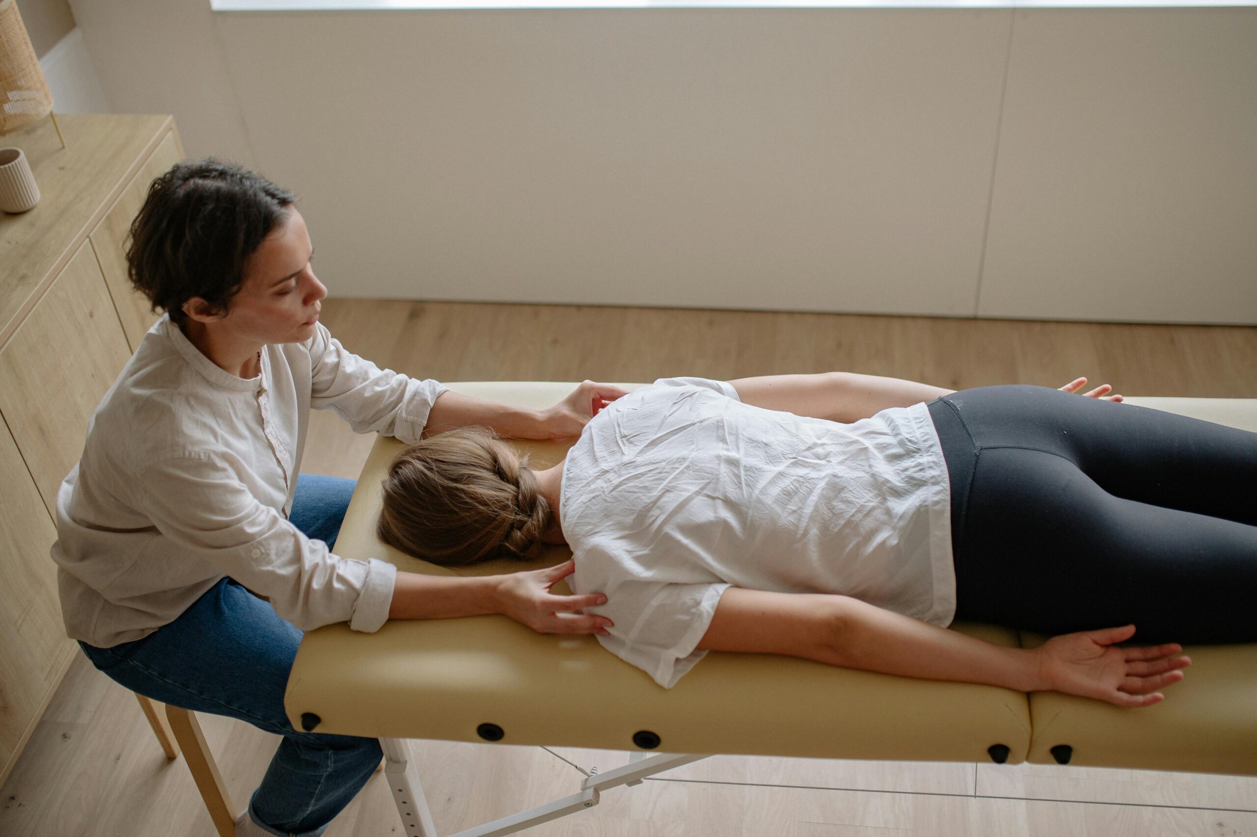 A therapist performs a chiropractic adjustment on a woman lying on a treatment table indoors.